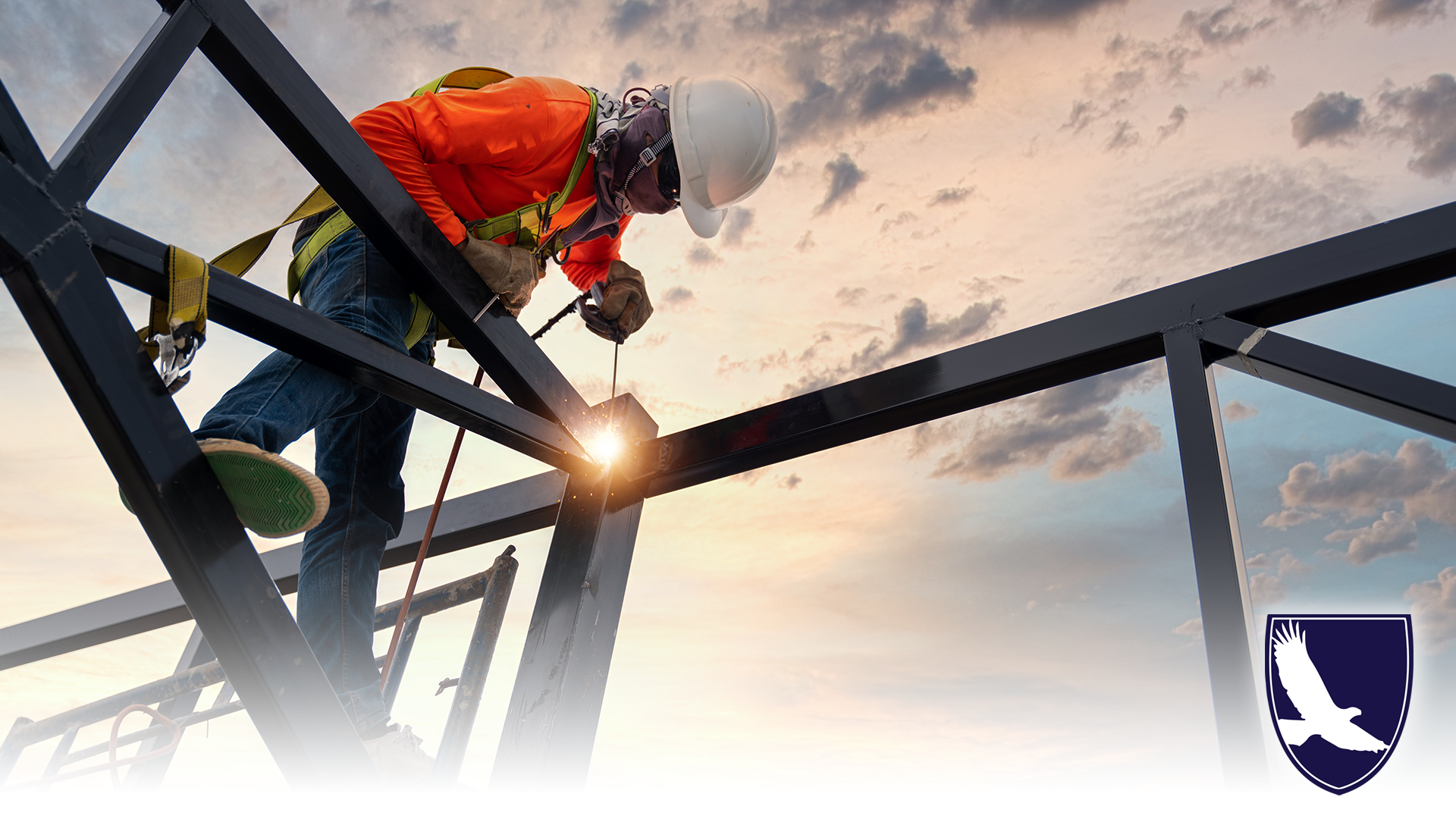 A welder is welding steel on a steel roof truss. Working at height equipment. Fall arrestor device for worker with hooks for safety body harness. Worker in construction